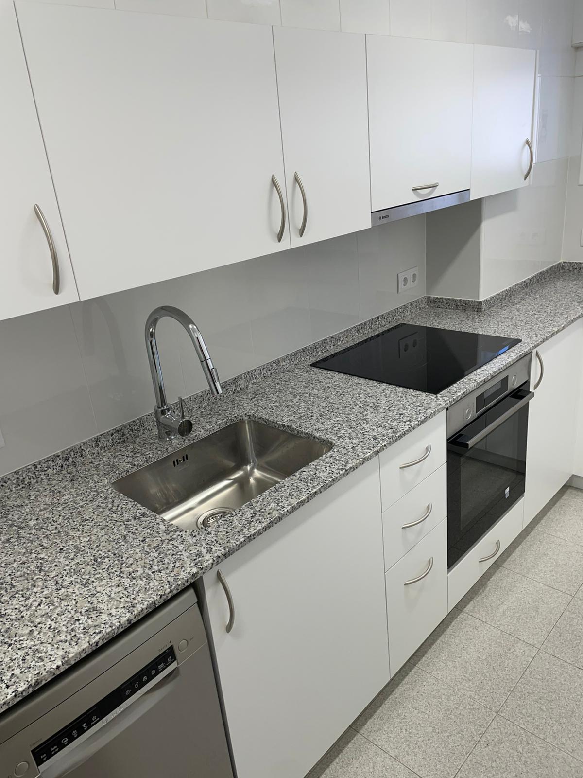 Cuina blanca amb encimera de granit i mobles llanternats